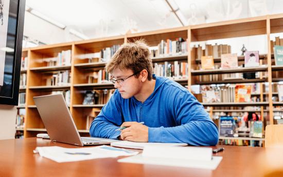 man in library sitting at table working at computer