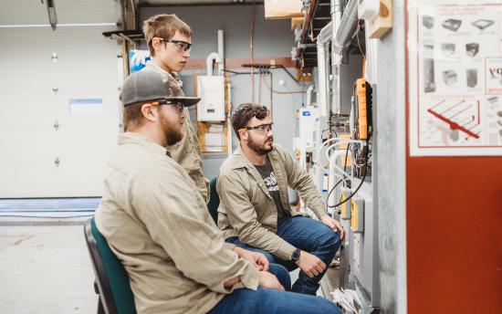 Three HVAC students are looking at a furnace in class