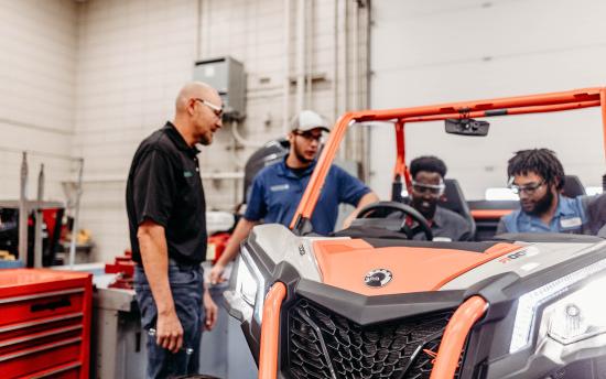 Three students from the Powersports program gathered around a small engine 